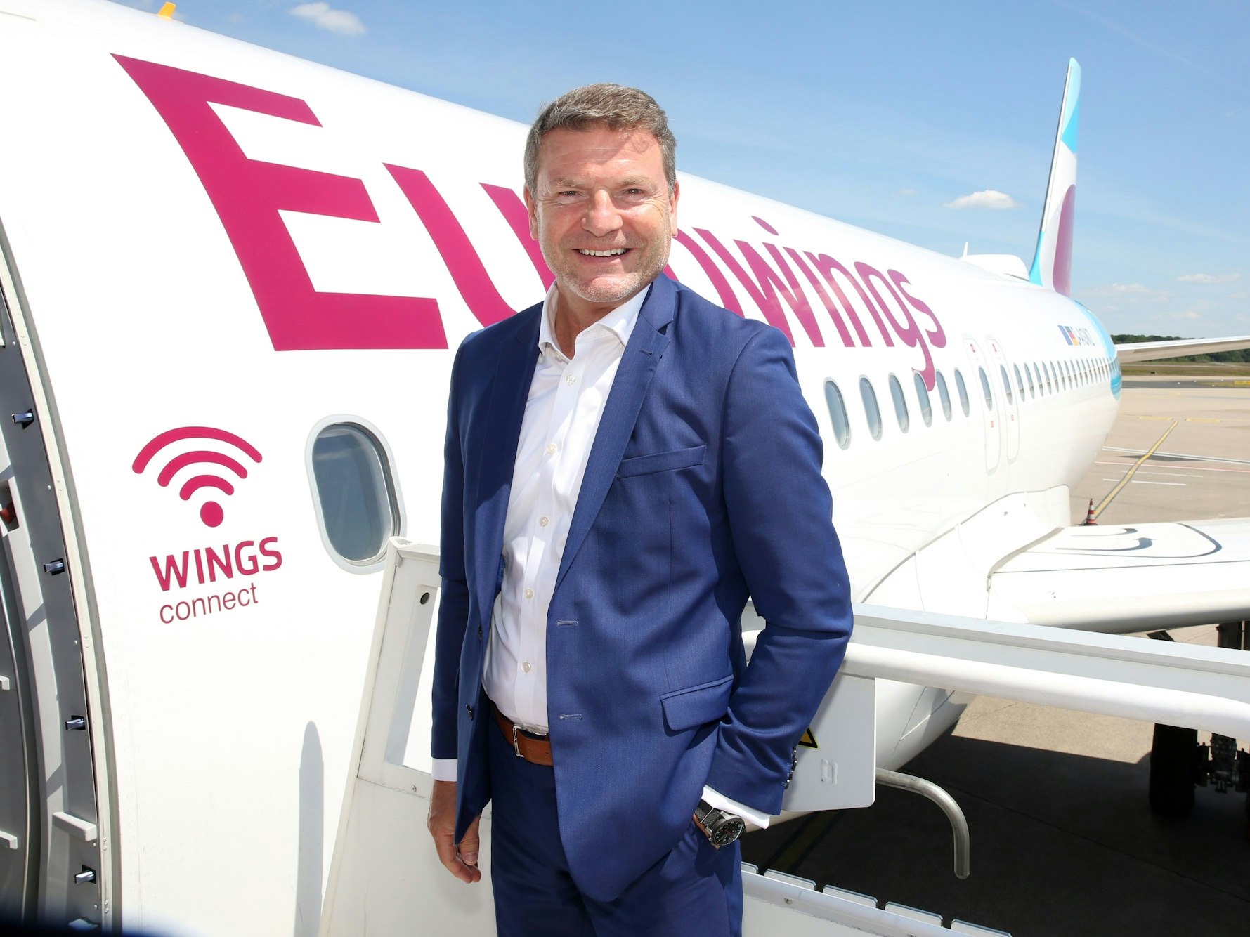 Eurowings-Chef Jens Bischof steht vor einer Eurowings-Maschine und lächelt in die Kamera.