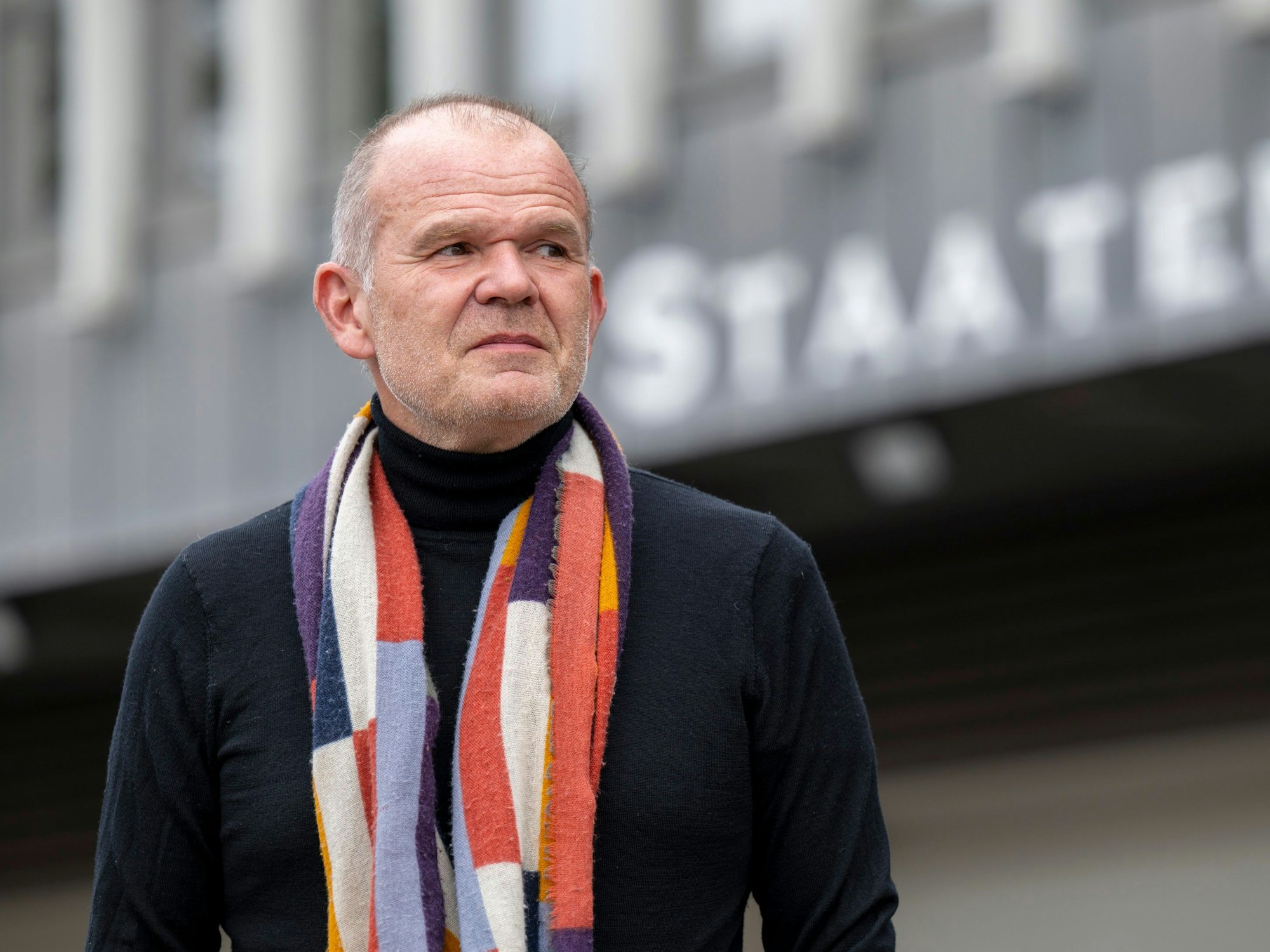 Francois-Xavier Roth steht mit Schal und Pullover vor dem Kölner Staatenhaus und schaut in die Ferne.