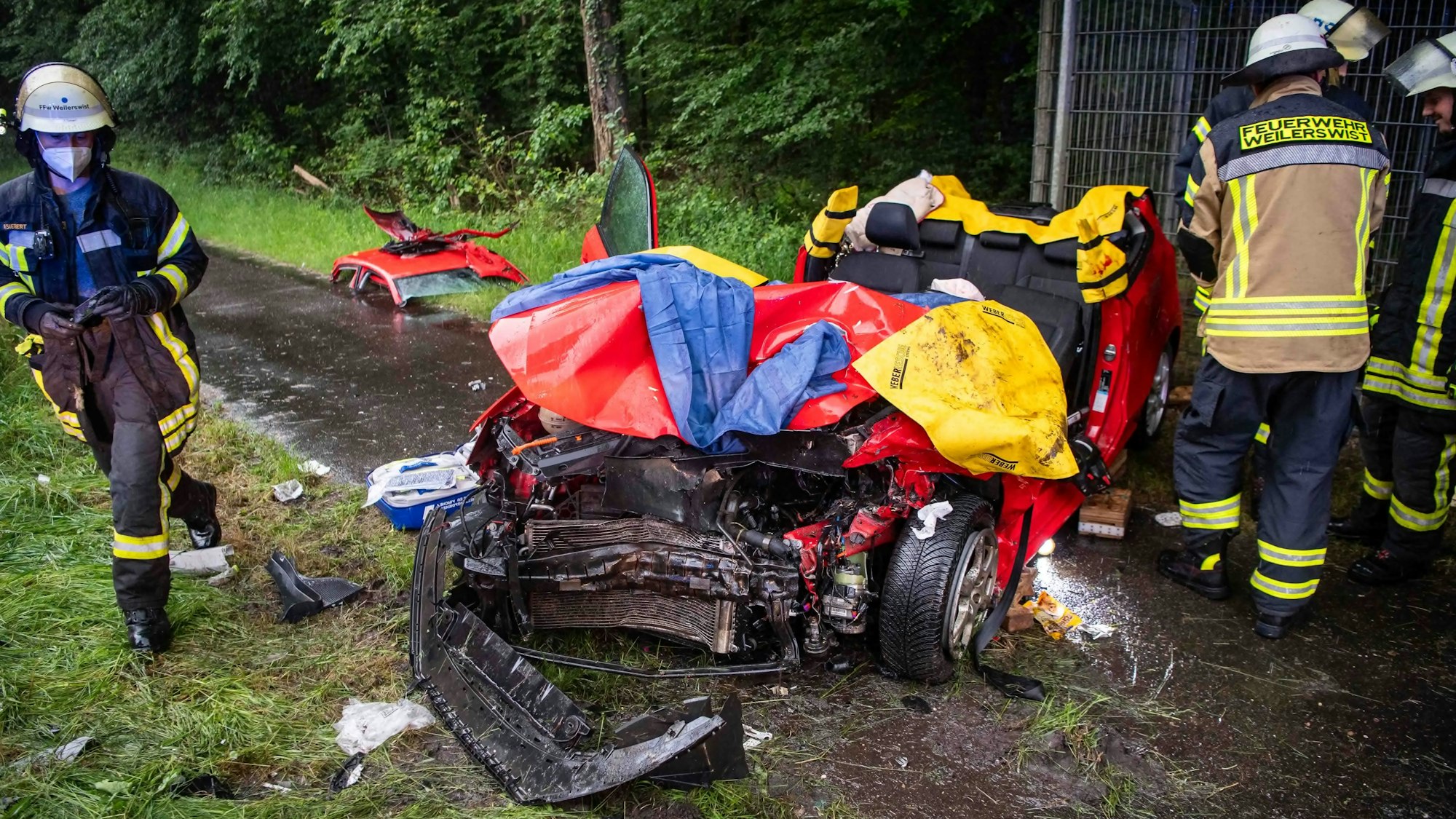 Ein Auto steht auf einem Gehweg, das abgetrennte Dach liegt ein paar Meter entfernt auf dem Boden. Die Stoßstange des Wagens ist abgerissen.