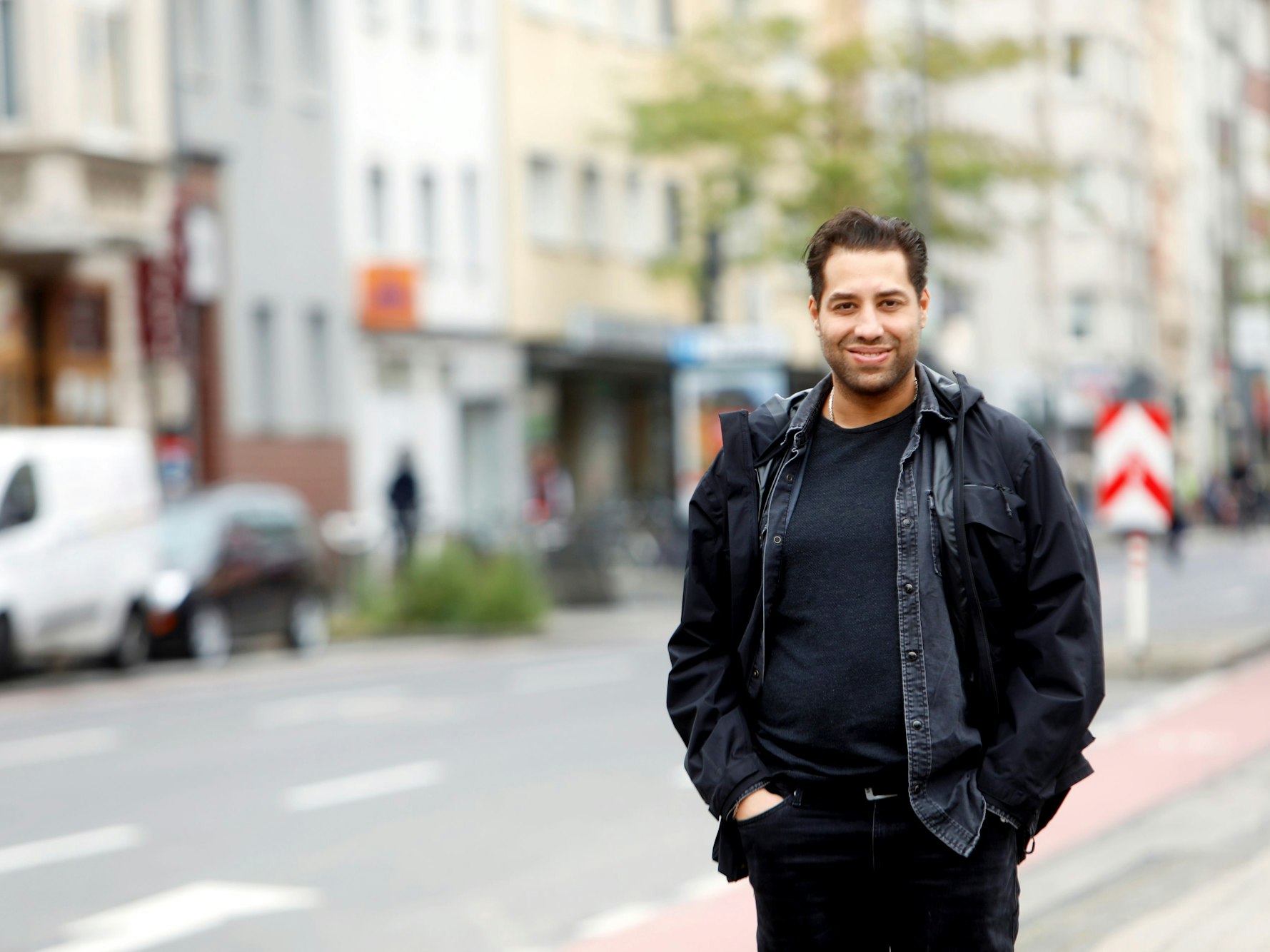 Der Kölner Schauspieler Kais Setti posiert auf der Straße und lächelt in die Kamera.