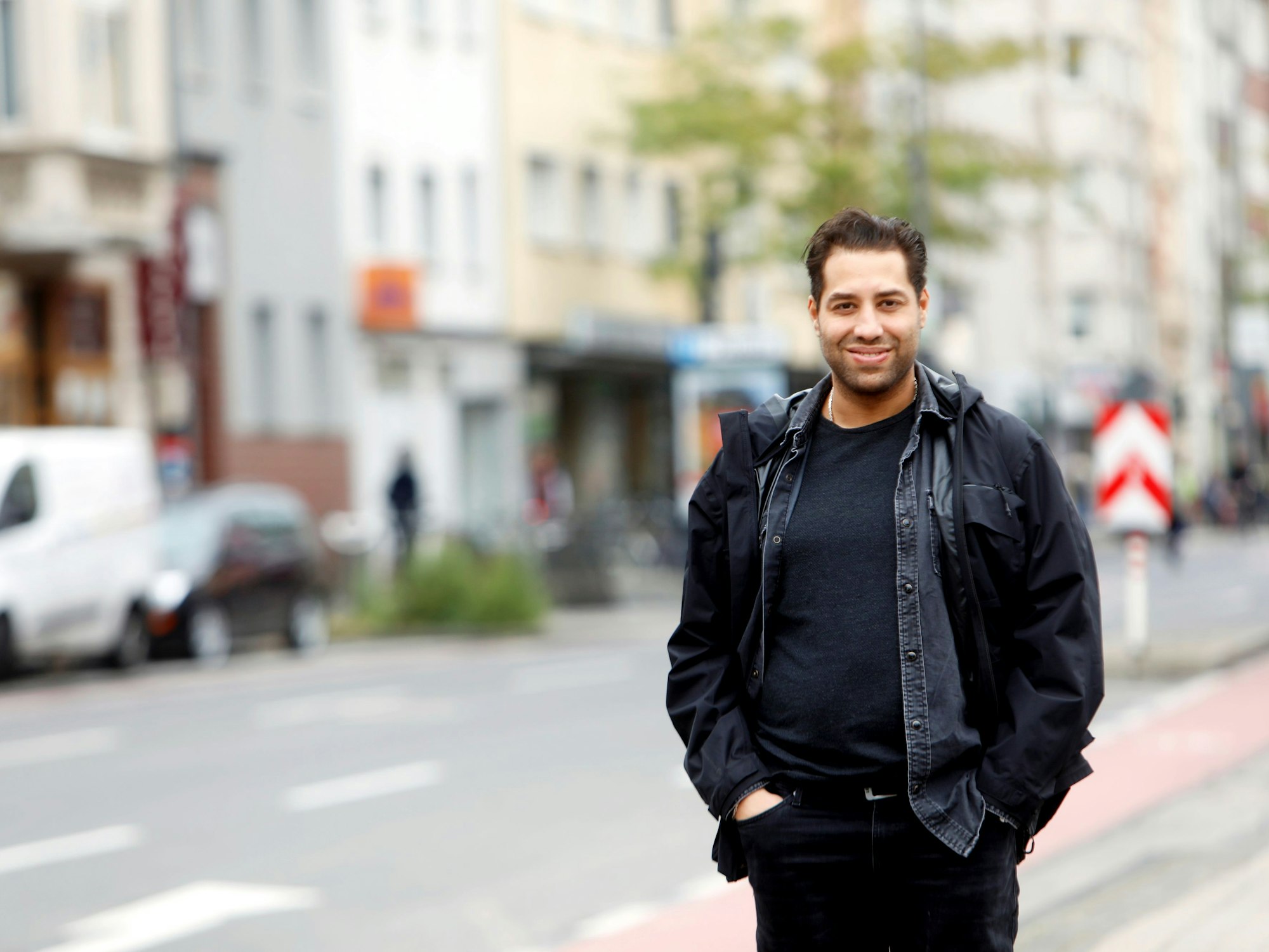 Der Kölner Schauspieler Kais Setti posiert auf der Straße und lächelt in die Kamera.
