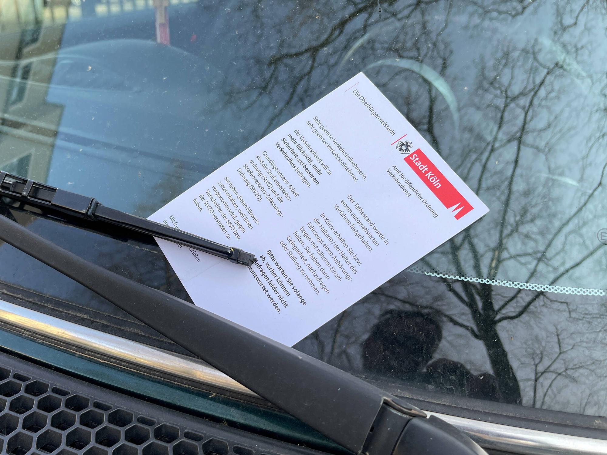 Ein Knöllchen klemmt hinter den Scheibenwischern eines Autos.