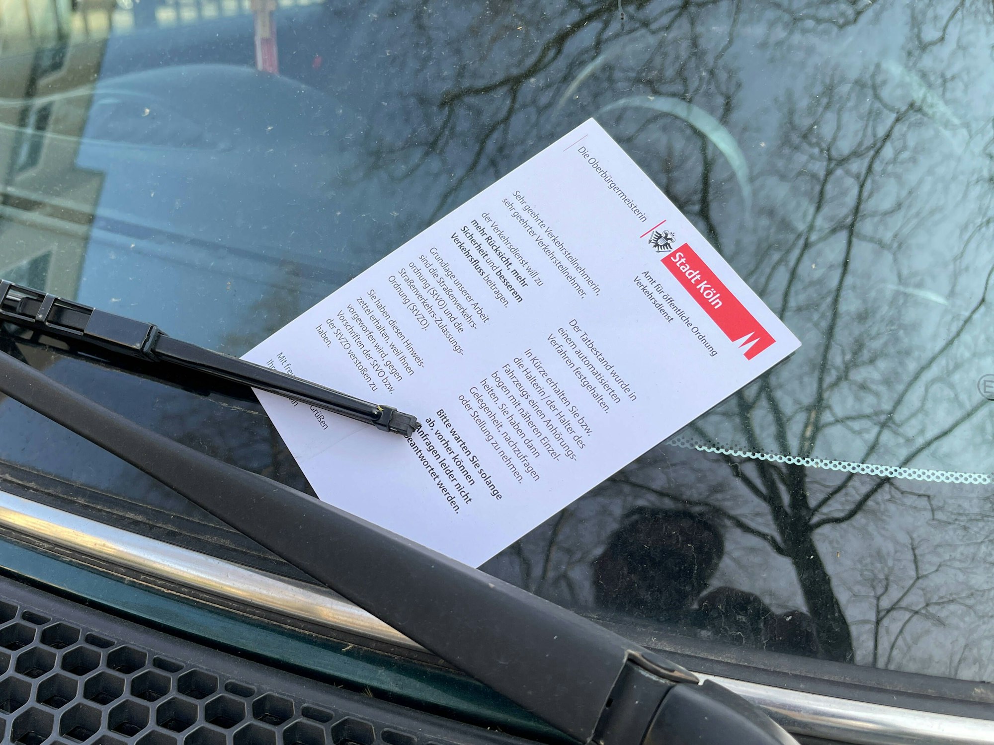 Ein Knöllchen klemmt hinter den Scheibenwischern eines Autos.