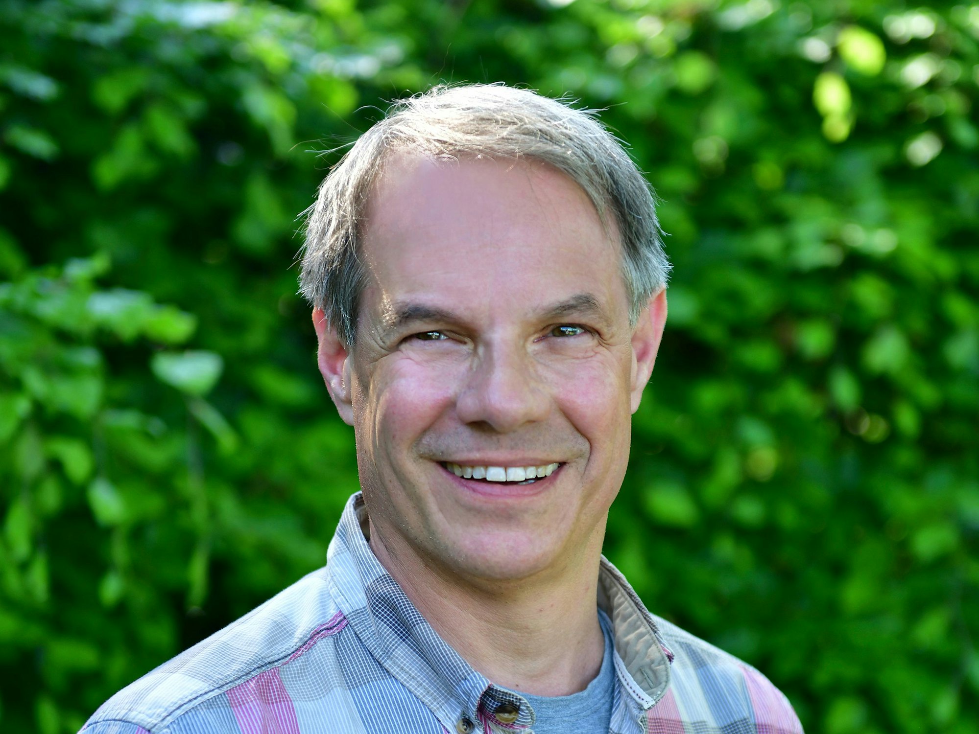 Biologe Dr. Markus Phlippen trägt ein Karohemd und lächelt freundlich vor einer Hecke.