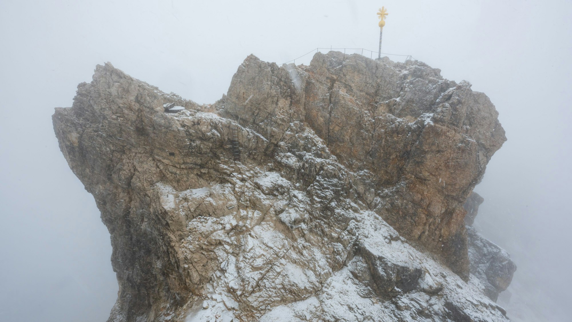Nebelwolken umhüllen bei Schneetreiben auf der Zugspitze (2962 Meter) die verschneite Aussichtsplattform mit dem Gipfelkreuz.