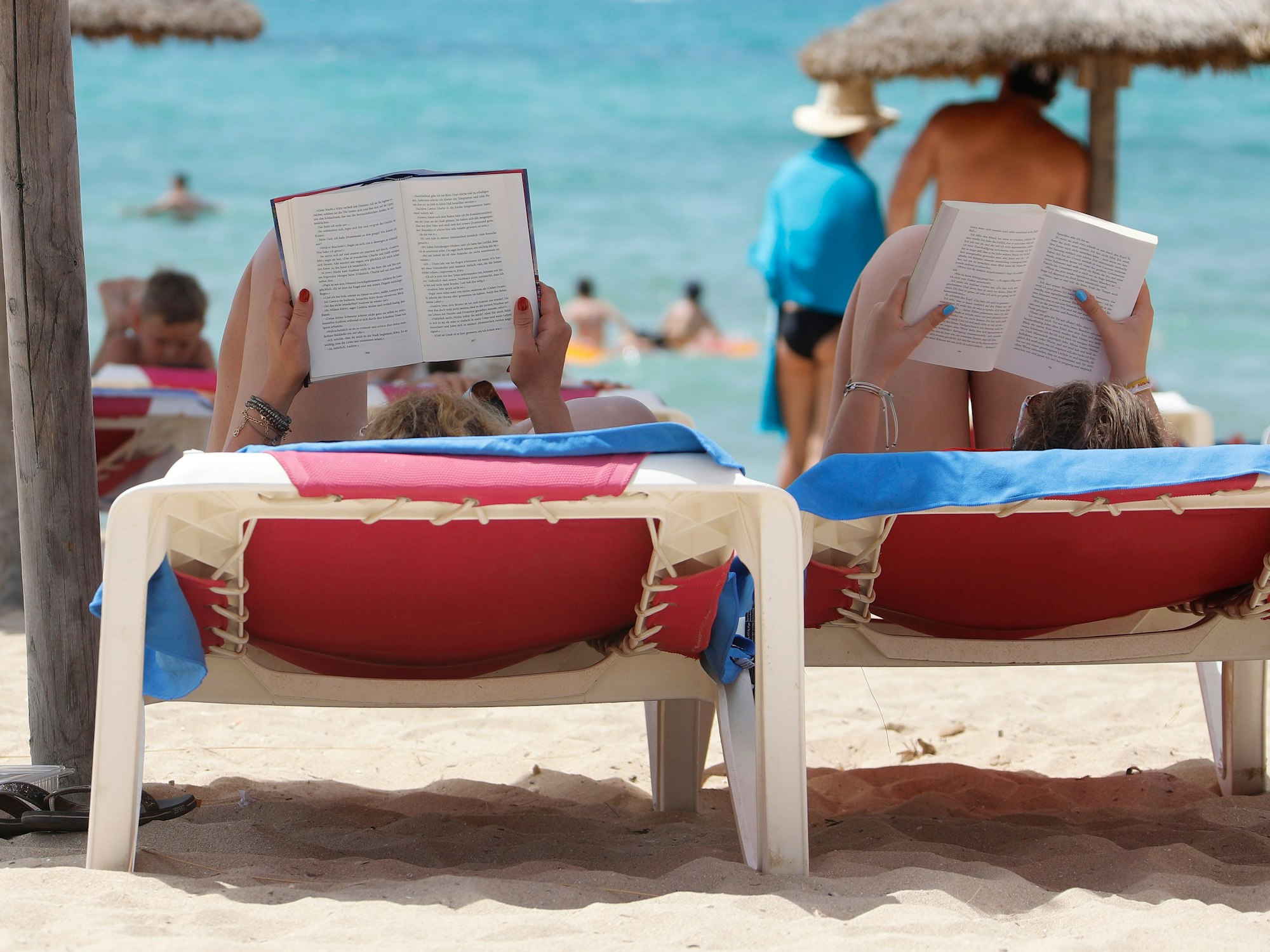 Zwei Frauen liegen am Strand „El Arenal“ auf Mallorca auf Liegestühlen und lesen in ihren Büchern, hier im August 2019.