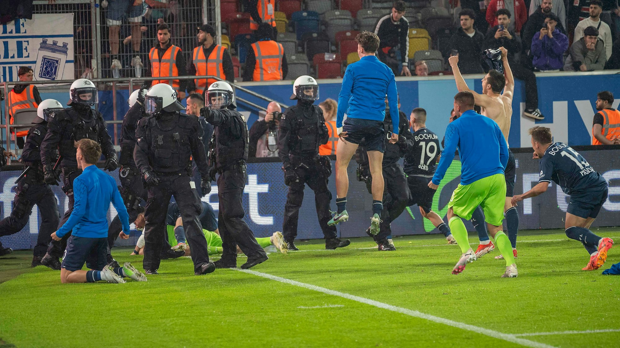 Die Spieler des VfL Bochum feiern den Bundesliga-Klassenerhalt in Gesellschaft etlicher Polizeikräfte in Einsatz-Montur.