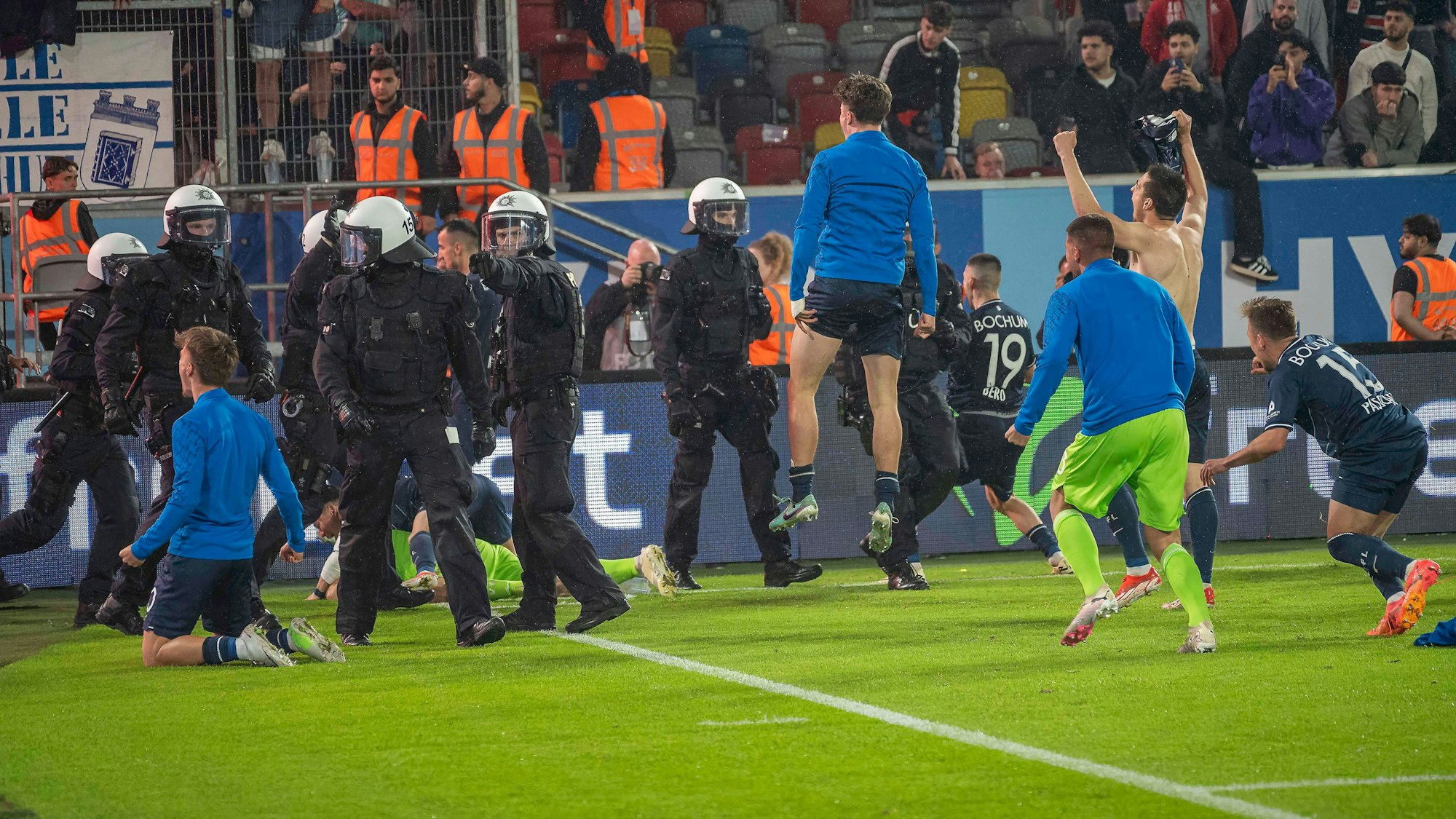 Die Spieler des VfL Bochum feiern den Bundesliga-Klassenerhalt in Gesellschaft etlicher Polizeikräfte in Einsatz-Montur.