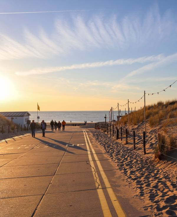 Menschen gehen an einer Verkehrsstraße am Noordwijk Strand im Sonnenuntergang spazieren