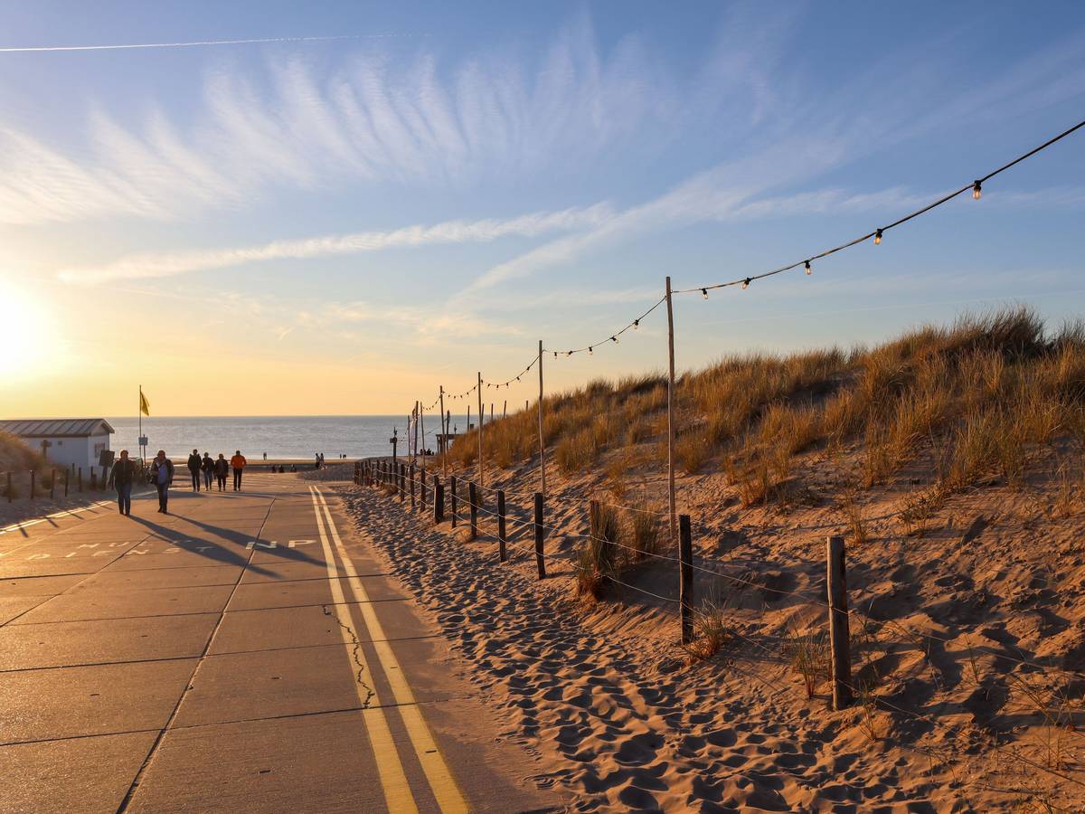 Menschen gehen an einer Verkehrsstraße am Noordwijk Strand im Sonnenuntergang spazieren