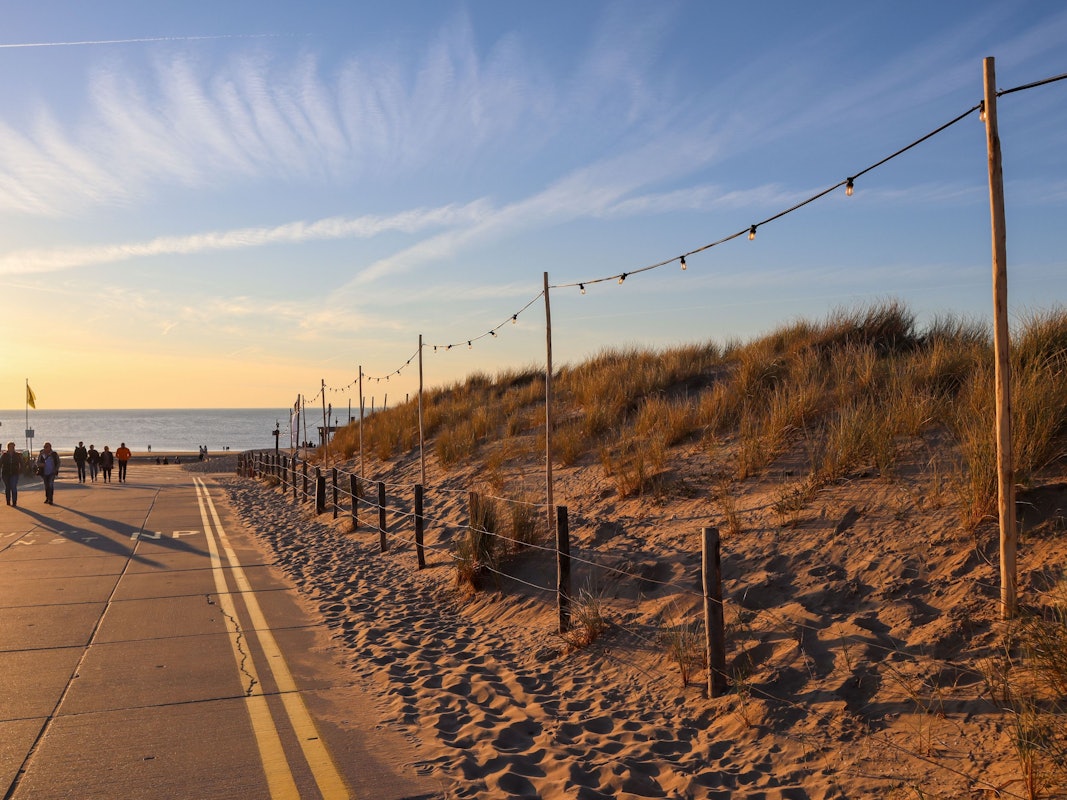Menschen gehen an einer Verkehrsstraße am Noordwijk Strand im Sonnenuntergang spazieren
