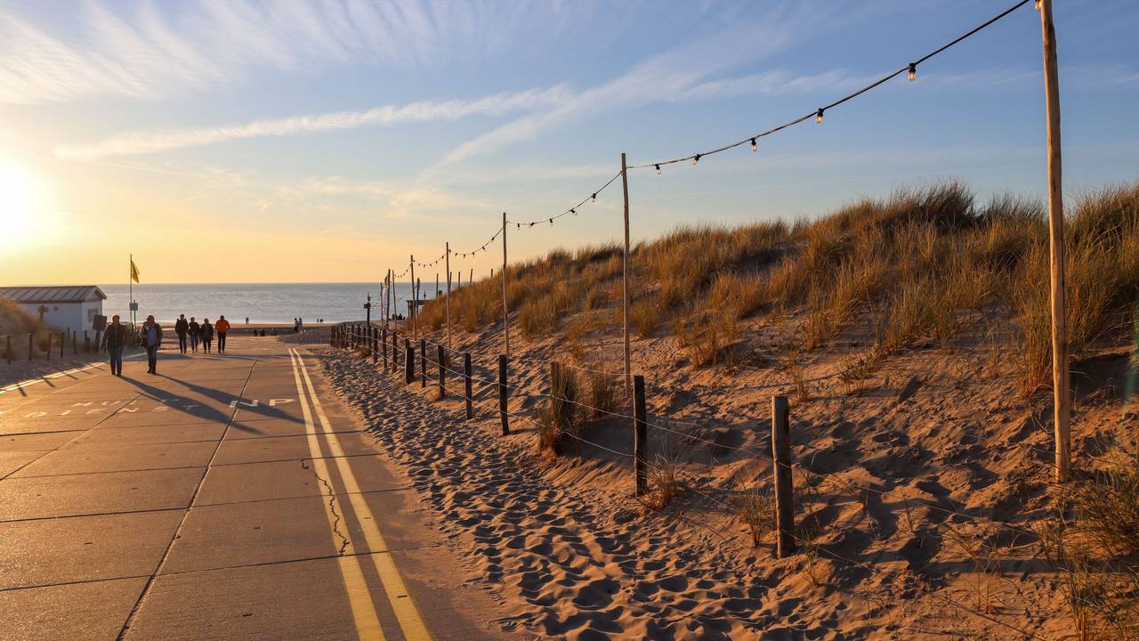 Menschen gehen an einer Verkehrsstraße am Noordwijk Strand im Sonnenuntergang spazieren