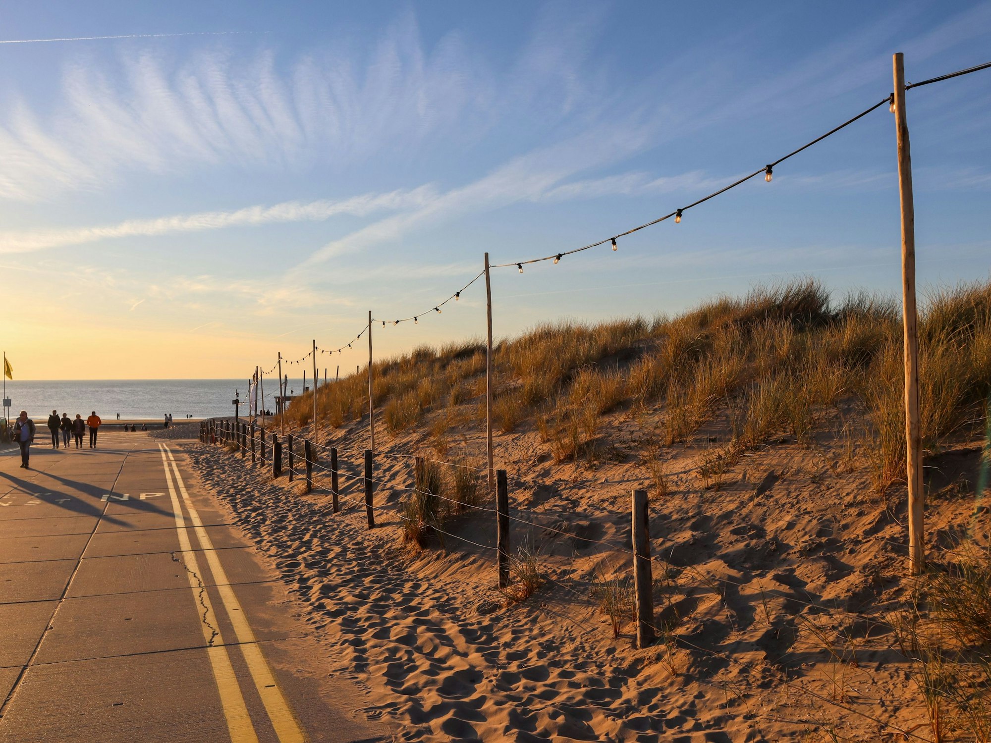 Menschen gehen an einer Verkehrsstraße am Noordwijk Strand im Sonnenuntergang spazieren