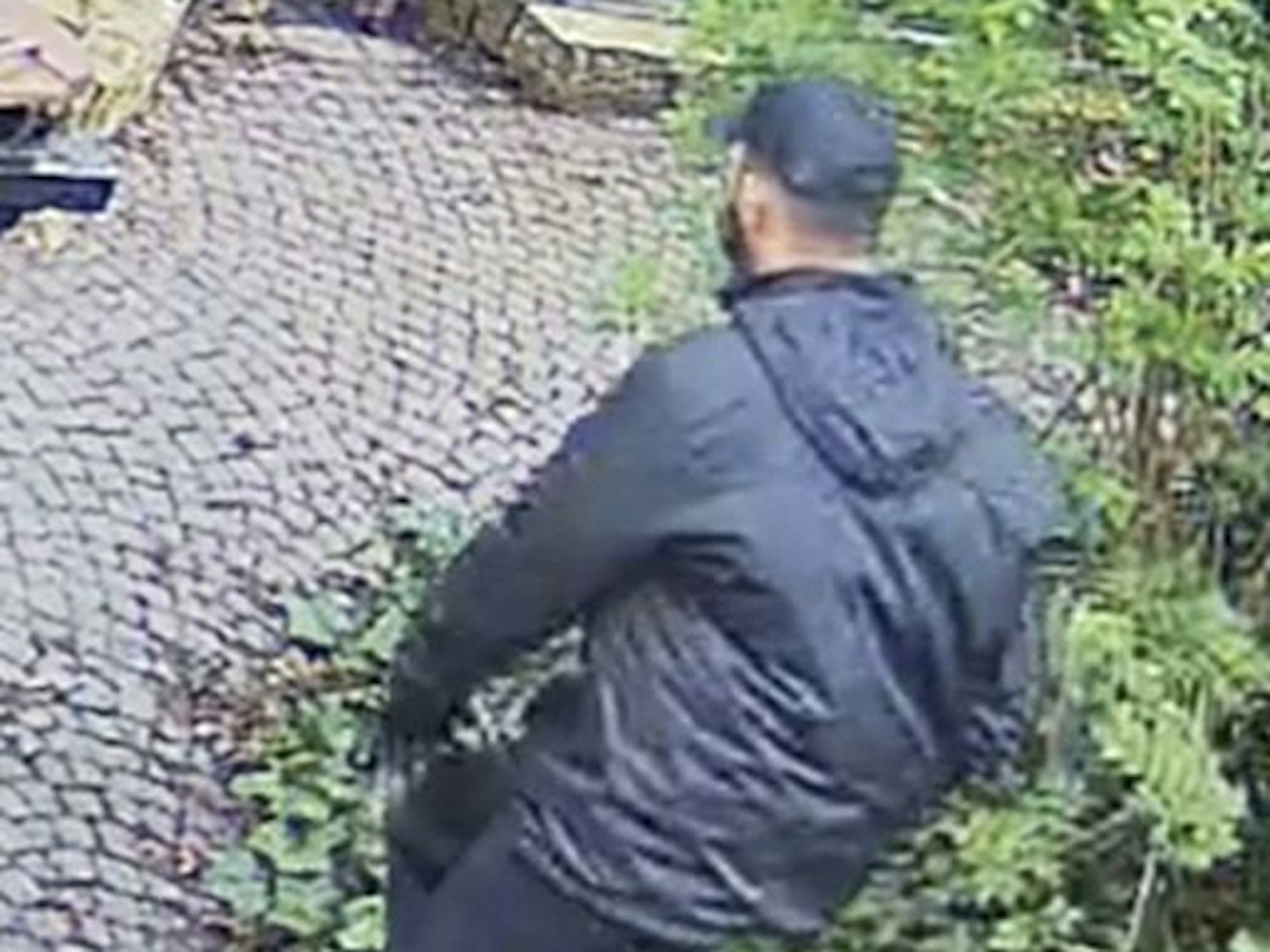 Mann mit dunkler Jacke und Kappe läuft durch einen Garten.