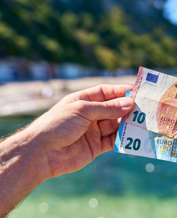 Dieses Symbolfoto zeigt: Ein Mann hält einen 20-Euro-Schein und einen 10-Euro-Schein an einem Strand in Italien in die Höhe.