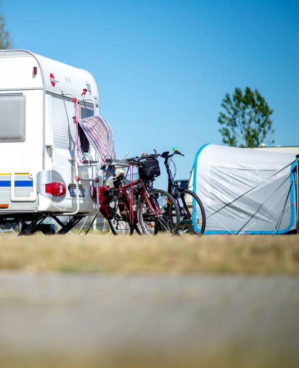 Hier zu sehen: Fahrräder stehen auf einem Campingplatz neben einem Wohnwagen.