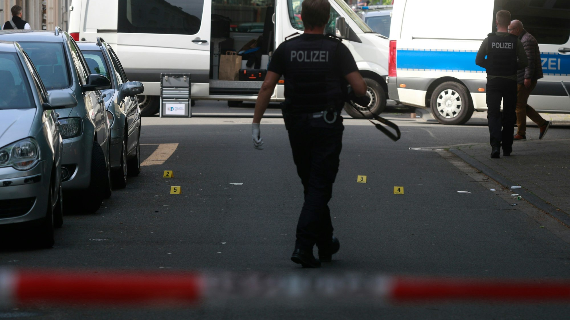 Die Straße ist mit Flatterband der Polizei abgesperrt, auf der Fahrbahn sind Spuren mit Schildchen nummeriert, ein Polizei mit Fotokamera läuft rum.