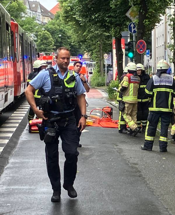 Rettungskräfte stehen an einem Auto, in dem eine Frau eingeklemmt ist, gegenüber steht eine Straßenbahn.