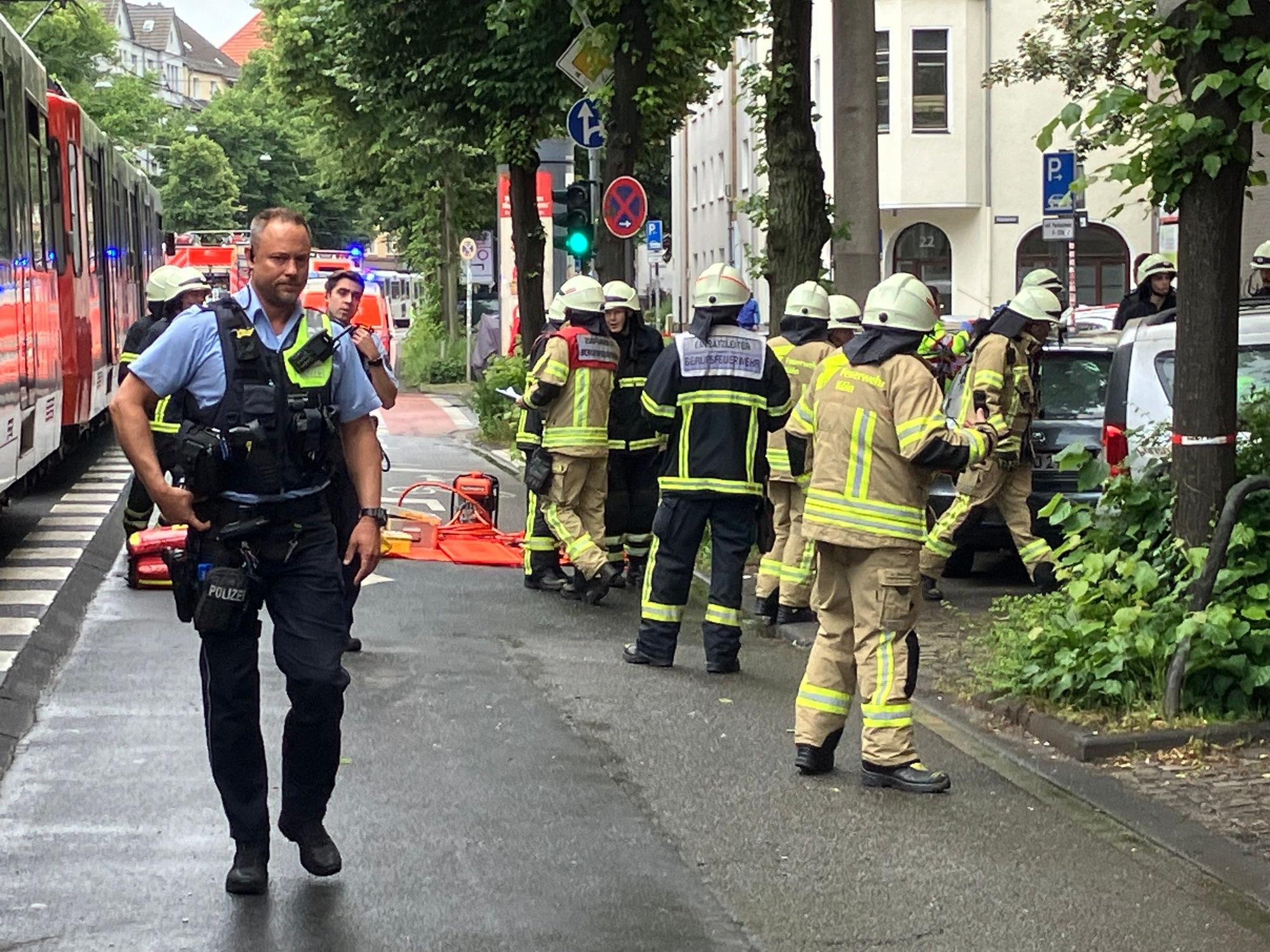 Rettungskräfte stehen an einem Auto, in dem eine Frau eingeklemmt ist, gegenüber steht eine Straßenbahn.