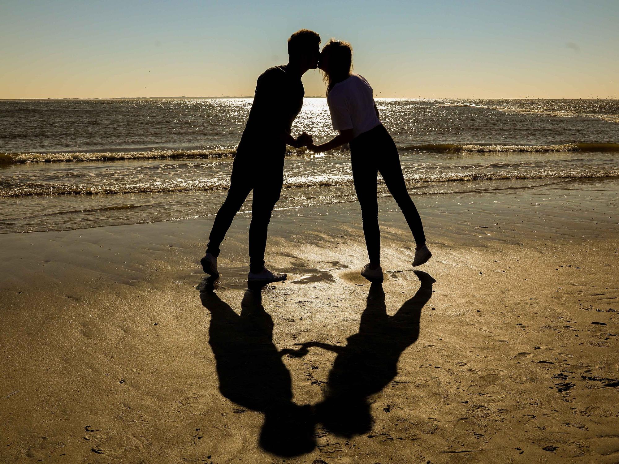 Ein Pärchen gibt sich am Strand einen Kuss.