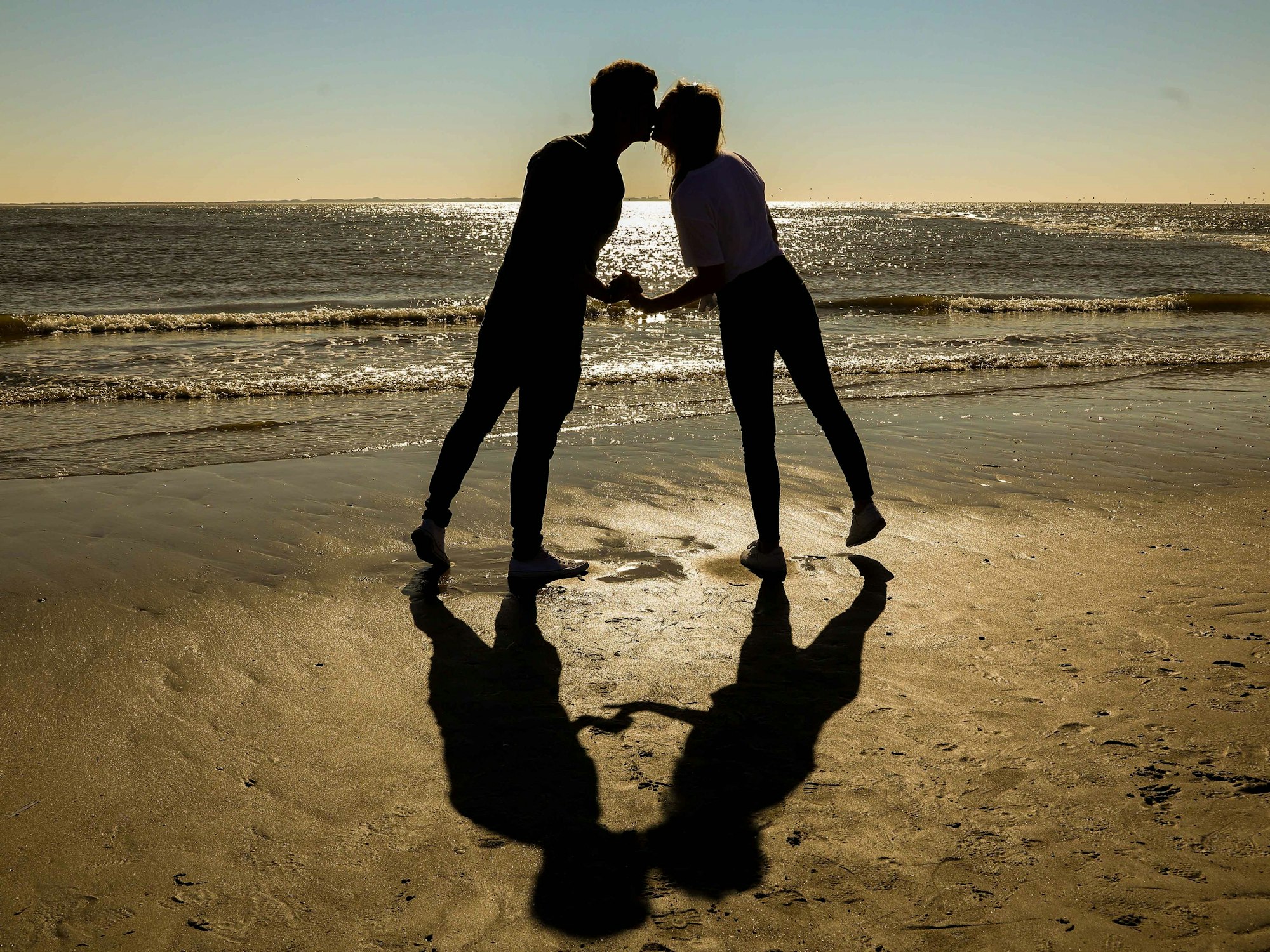 Ein Pärchen gibt sich am Strand einen Kuss.
