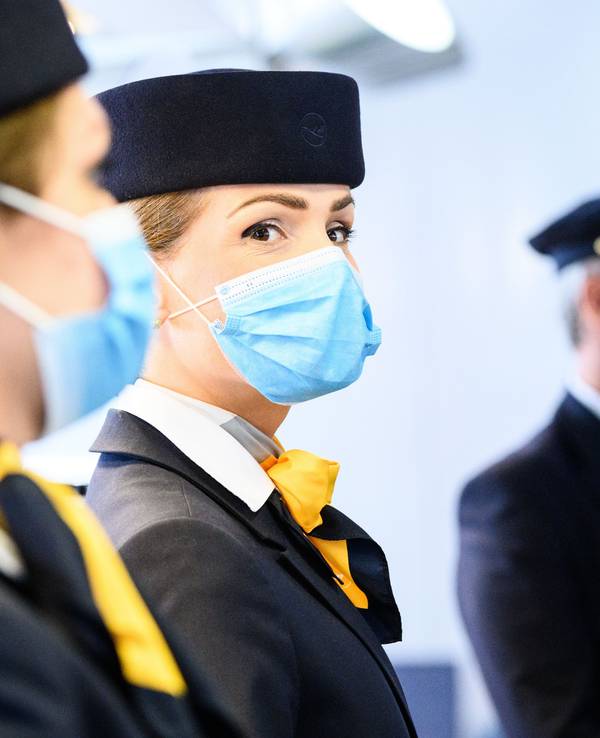 Zwei Flugbegleiterinnen und ein Pilot der deutschen Fluggesellschaft Lufthansa stehen am Flughafen.