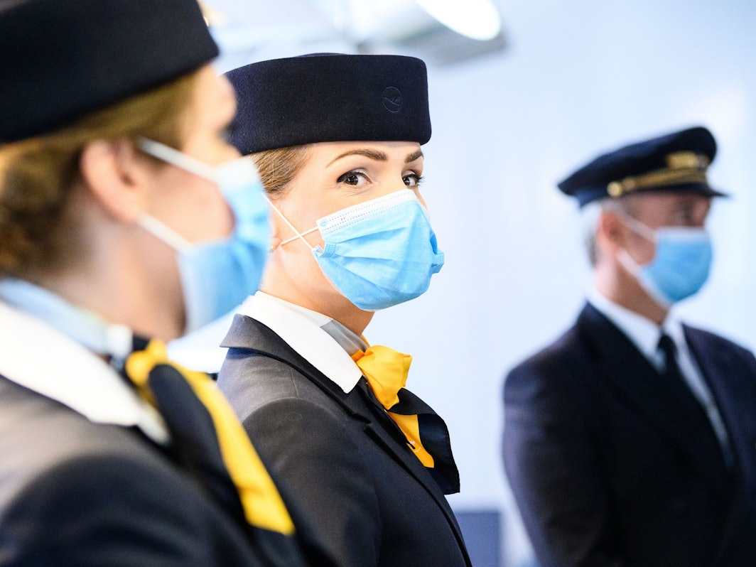 Zwei Flugbegleiterinnen und ein Pilot der deutschen Fluggesellschaft Lufthansa stehen am Flughafen.