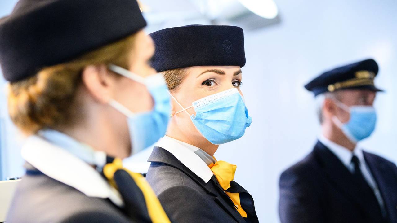Zwei Flugbegleiterinnen und ein Pilot der deutschen Fluggesellschaft Lufthansa stehen am Flughafen.