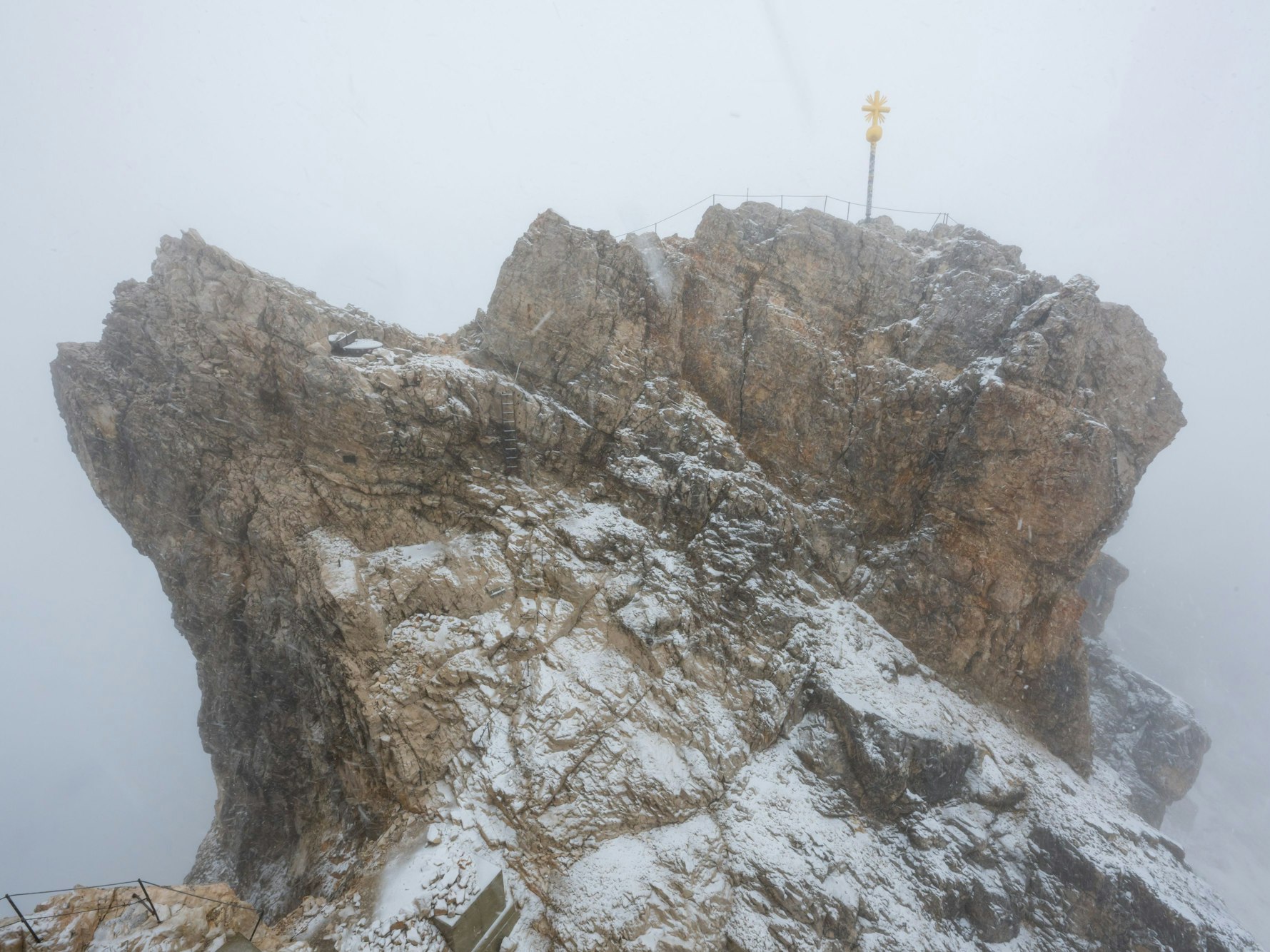 Nebelwolken umhüllen im Juli 2023 bei Schneetreiben auf der Zugspitze (2962 Meter) die verschneite Aussichtsplattform mit dem Gipfelkreuz.