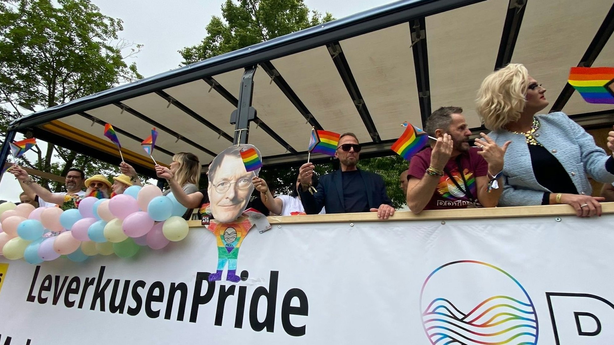 Menschen stehen auf einem Wagen und haben Fähnchen in den Händen.