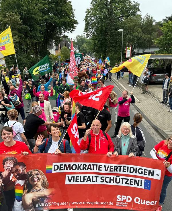 Menschen demonstrieren auf der Straße, mehrere tragen ein Plakat mit der Aufschrift „Demokratie verteidigen, Vielfalt schützen“.
