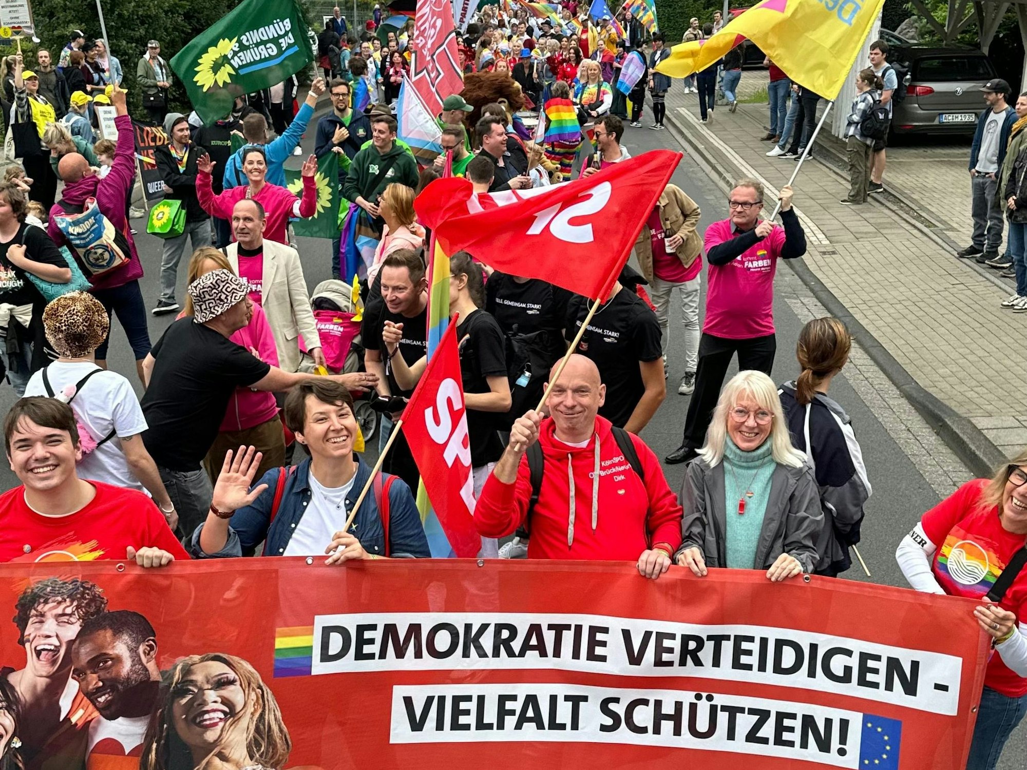 Menschen demonstrieren auf der Straße, mehrere tragen ein Plakat mit der Aufschrift „Demokratie verteidigen, Vielfalt schützen“.