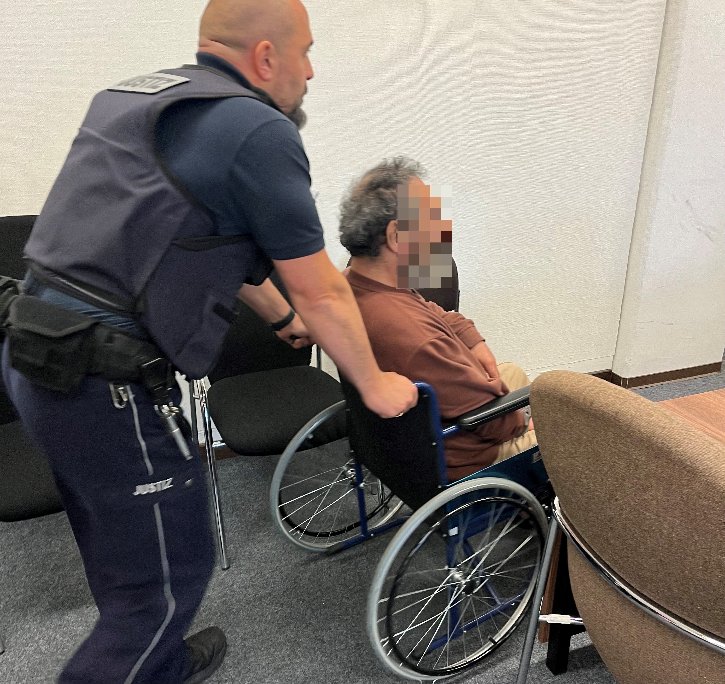Ein Wachtmeister schiebt einen Mann, der im Rollstuhl sitzt.