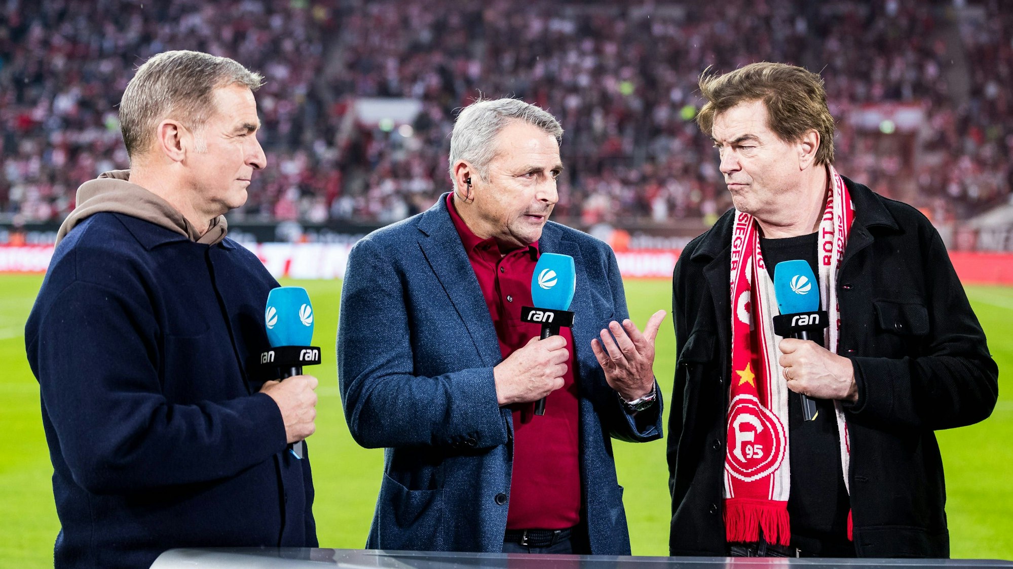 Stefan Kuntz steht mit SAT.1-Mikro neben Fortuna-Sportboss Klaus Allofs und Campino.