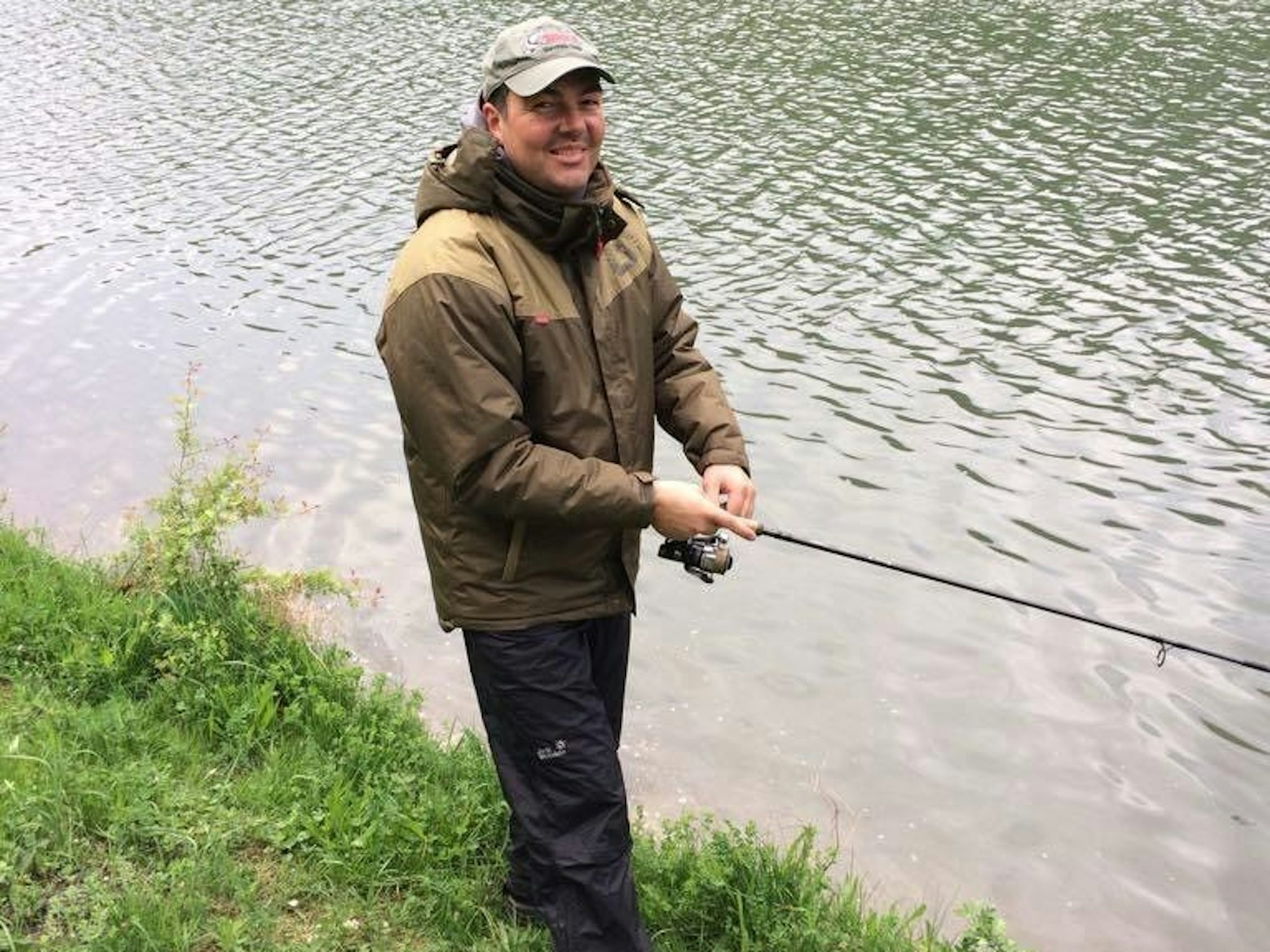 Ein Mann steht an einem Gewässer und angelt.