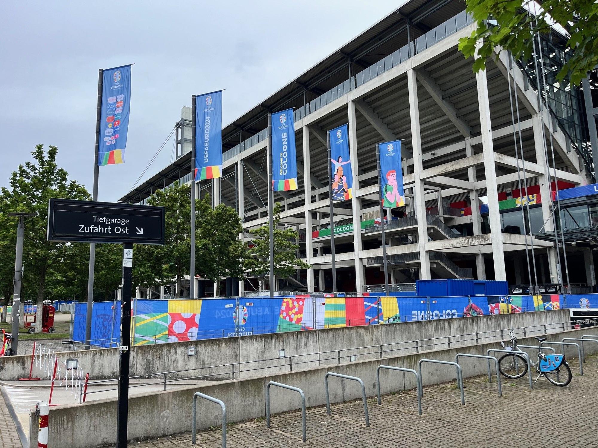 Blick von außen auf das Stadion in Köln, das mit EM-Fahnen in den Farben der Uefa geschmückt ist.