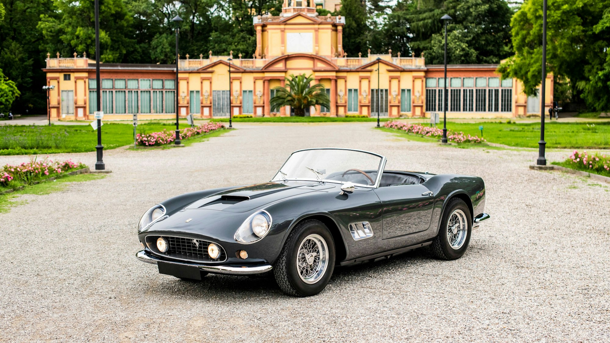 Der erste 1960 Ferrari 250 GT SWB California Spider steht vor einem Gebäude.