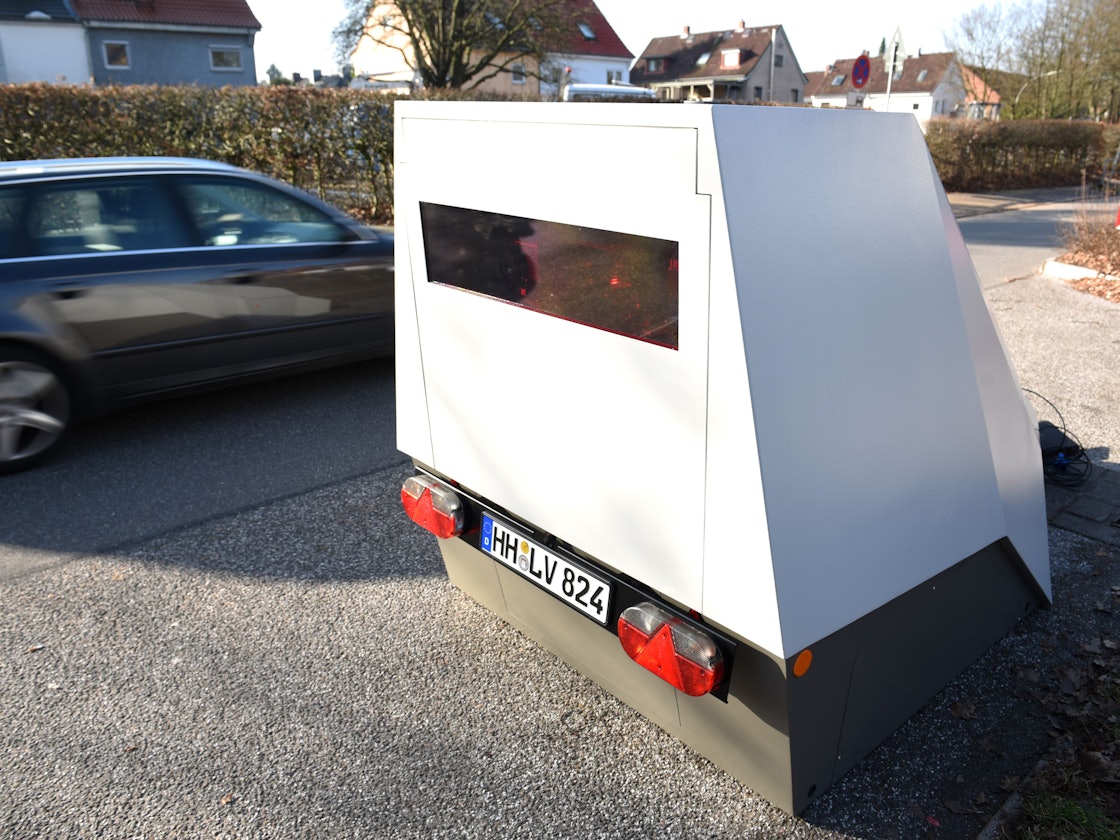 Ein Anhänger zur mobilen Geschwindigkeitsüberwachung steht am Straßenrand.