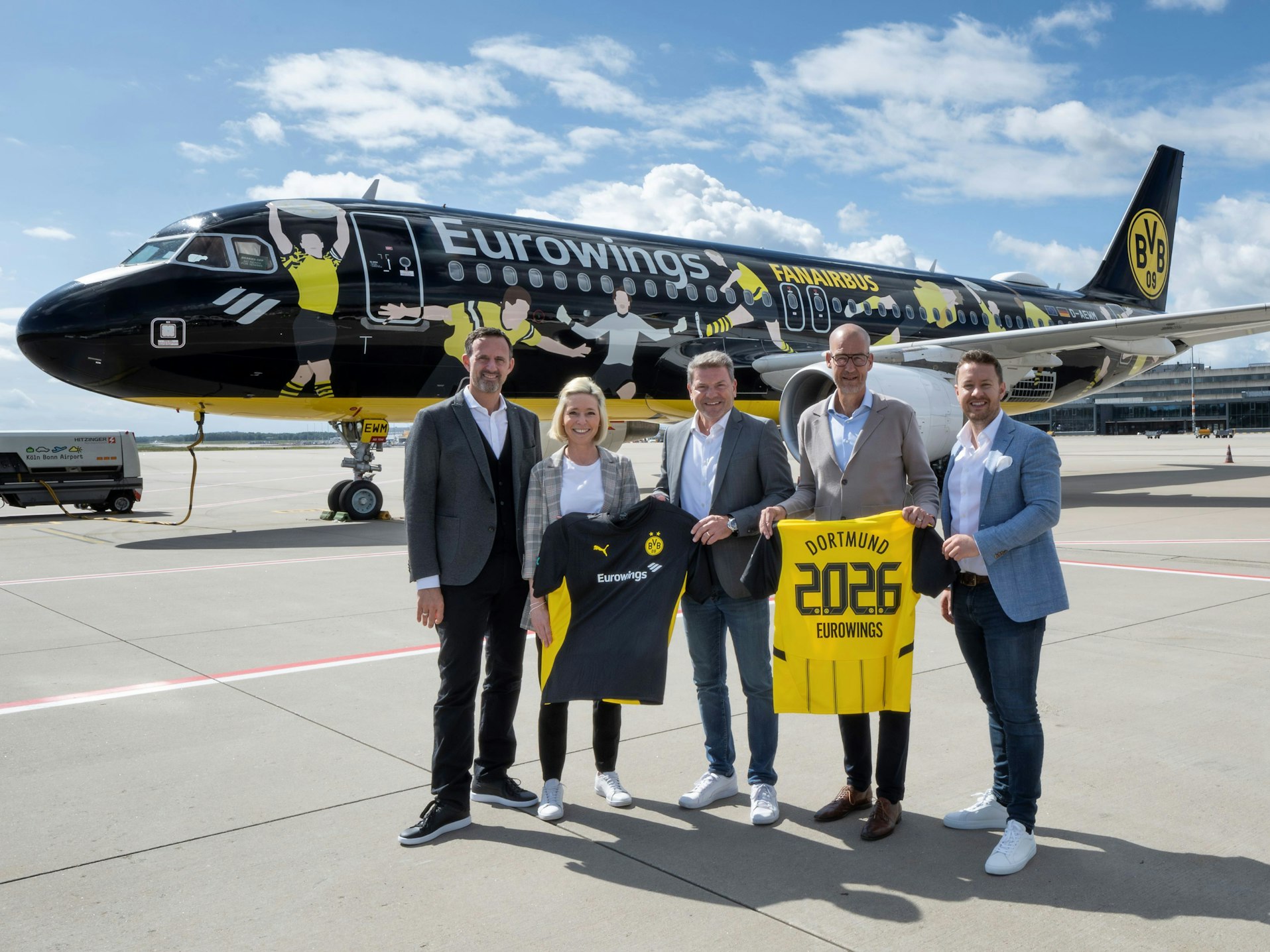 Vier Männer und eine Frau halten vor dem neuen BVB-Flugzeug ein Trikot des Vereins in die Kamera und lächeln.