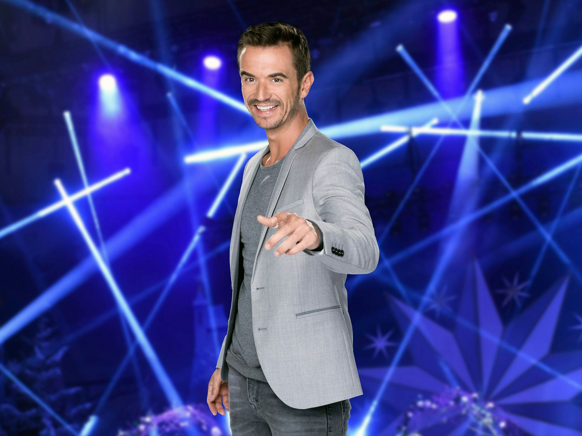 Das Foto zeigt ARD-Moderator Florian Silbereisen lächelnd. Im Hintergrund ist eine Lichtershow zu sehen.