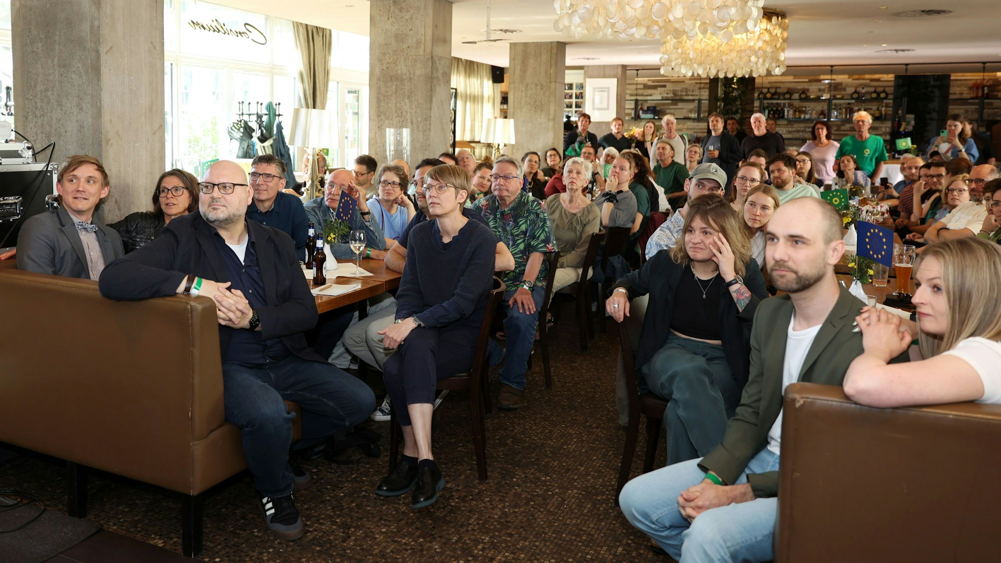 Eine Menschengruppe verfolgt bei einer Wahlparty auf einem Fernseher das Ergebnis.