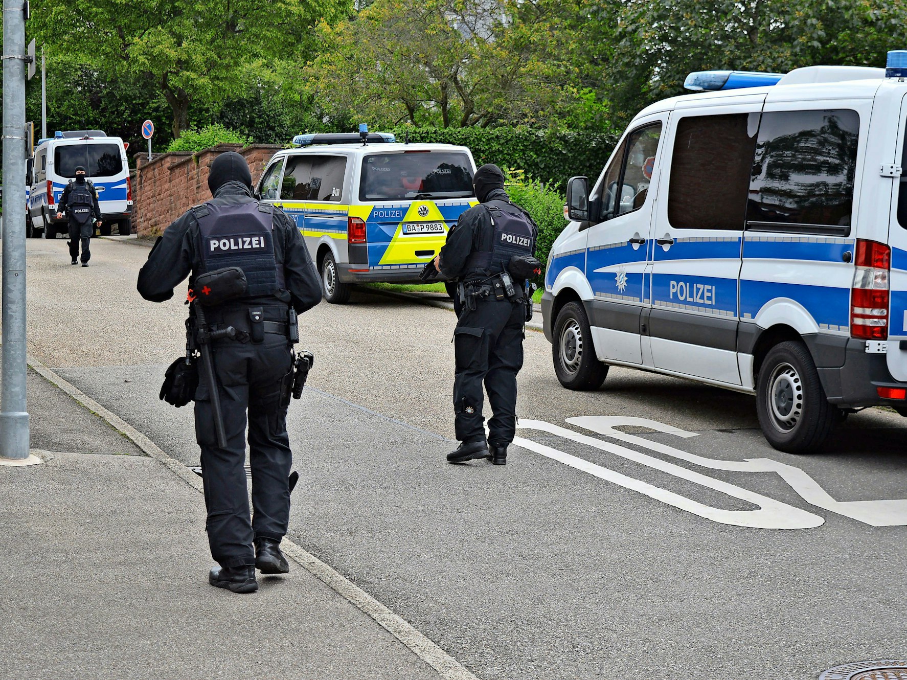 Polizisten bei einer Razzia, hinter ihnen sind die Streifenwagen zu sehen.