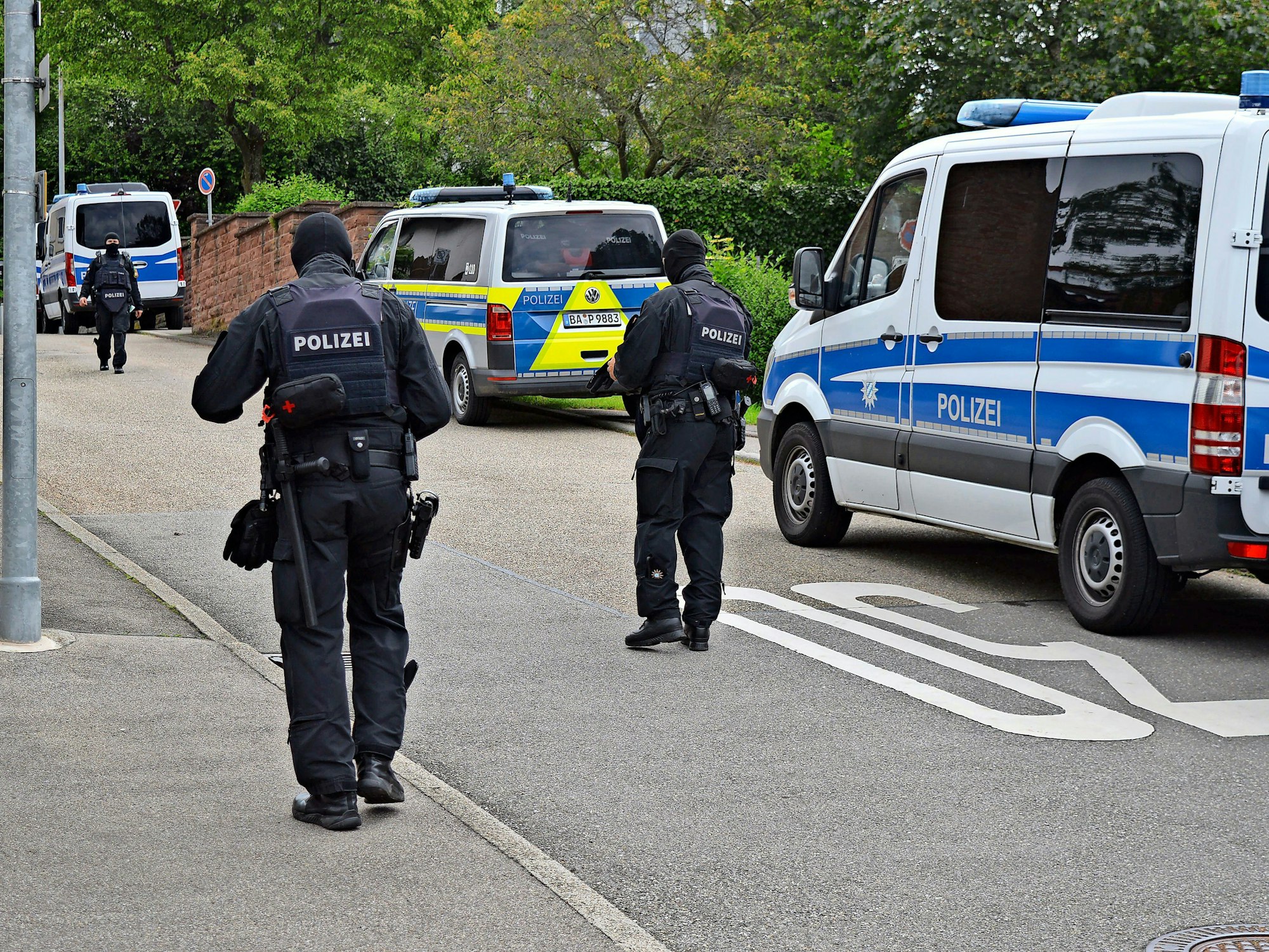 Polizisten bei einer Razzia, hinter ihnen sind die Streifenwagen zu sehen.
