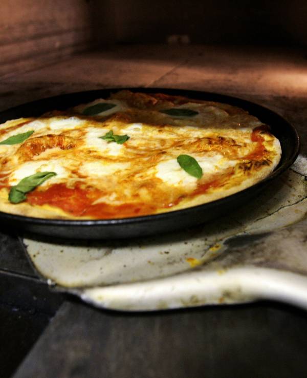 Ein Pizzabäcker holt mit einem Schieber eine frisch zubereitete typische Pizza Margherita, belegt mit Mozzarella und Basilikum, aus einem Pizzaofen in Frankfurt am Main (Symbolbild).