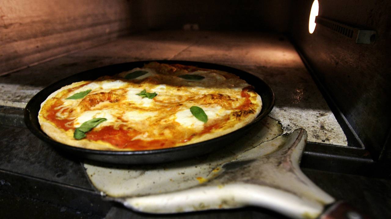 Ein Pizzabäcker holt mit einem Schieber eine frisch zubereitete typische Pizza Margherita, belegt mit Mozzarella und Basilikum, aus einem Pizzaofen in Frankfurt am Main (Symbolbild).