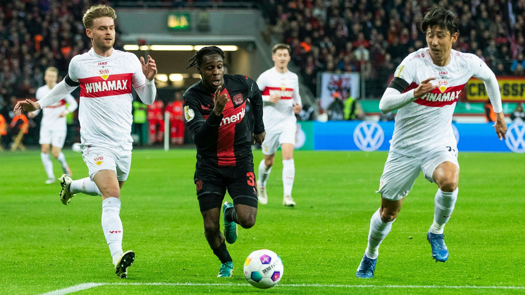 Bayer-Profi Jeremie Frimpong (M.) sprintet dem Ball hinterher, Maximilian Mittelstädt (l.) und Hiroki Ito versuchen ihn zu stören.