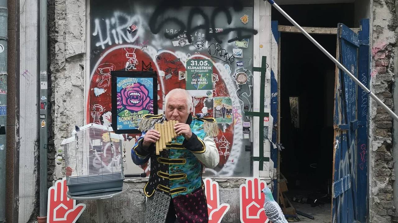 Ein Mann it ner Flöte steht vor einem Haus.