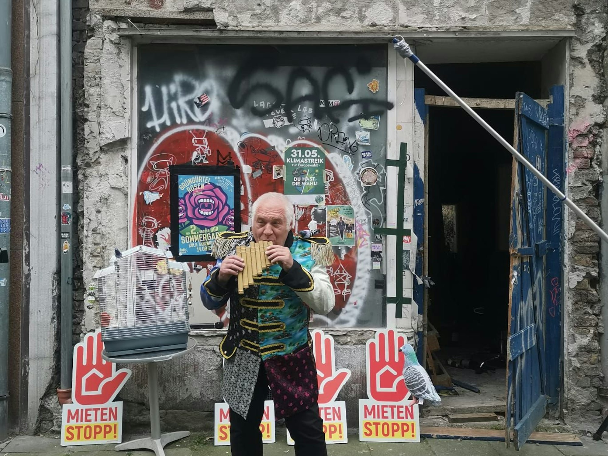 Ein Mann it ner Flöte steht vor einem Haus.