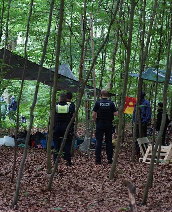 Polizisten stehen in einem Waldstück und sprechen mit Menschen.
