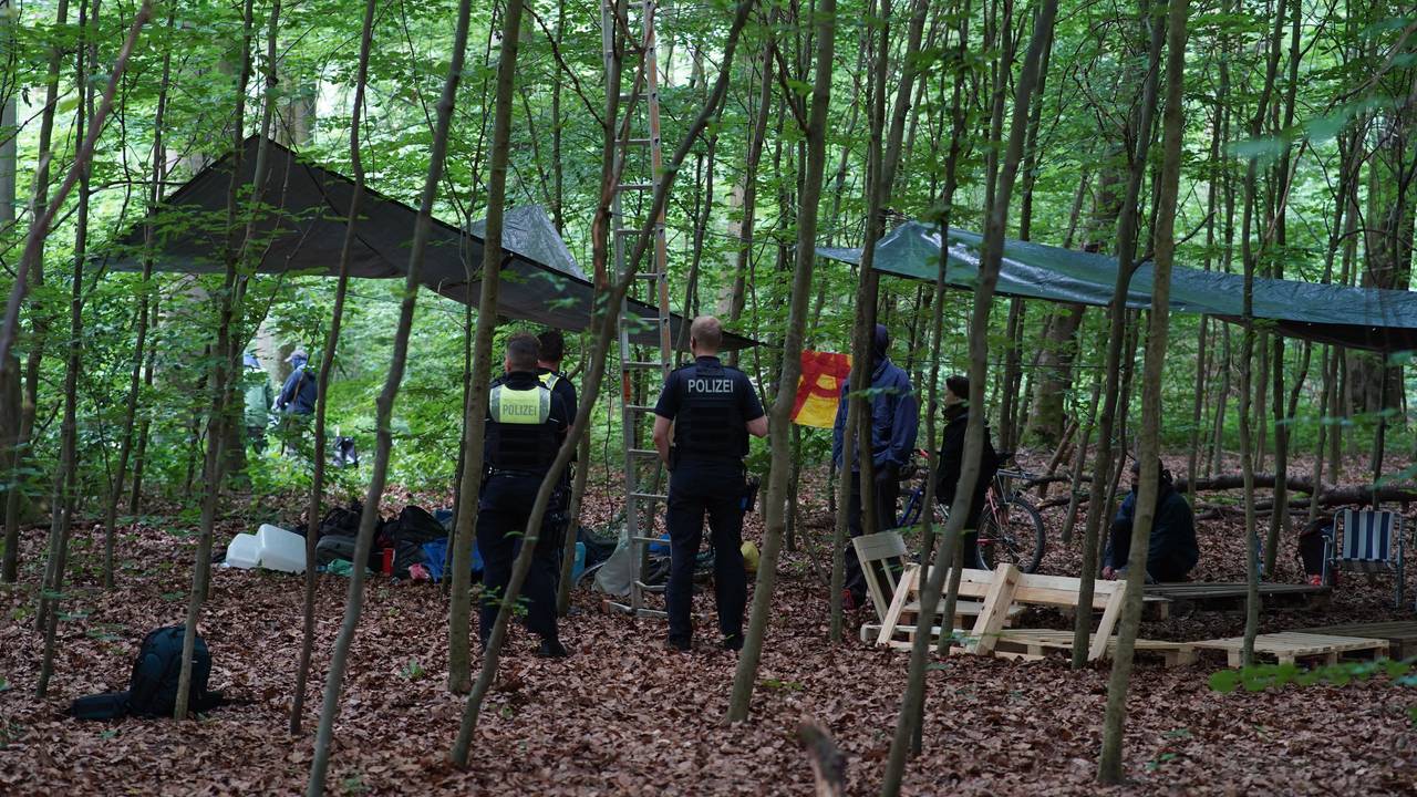 Polizisten stehen in einem Waldstück und sprechen mit Menschen.